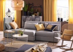 A medium sized living room furnished with a three-seat sofa combination in plain gray and with black/beige pattern, that can be converted into a bed. Combined with a white storage table and a modern rocking-chair in handwoven rattan.