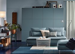 A medium sized living room furnished with a turquoise three-seat sofa and a footstool in the same color. Combined with a white storage table and a large storage combination in gray-turquoise.